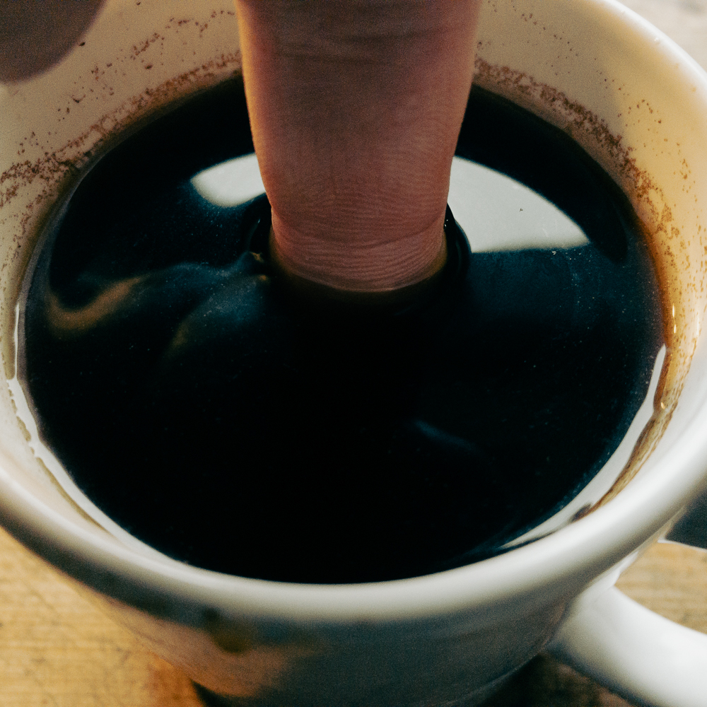 Eine Tasse Kaffee, in die ein Finger gehalten wird, um zu beweisen, dass der Kaffee kalt ist.
